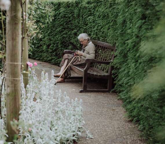 starsza kobieta czytająca książkę na ławce w parku